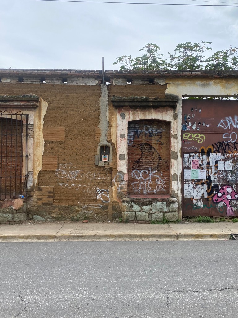 Wide street view of bold pastel drawing of framed artwork of a chile serrano hung in the streets of Oaxaca City. This was left behind as a part of the experimental installation and performance of free art.